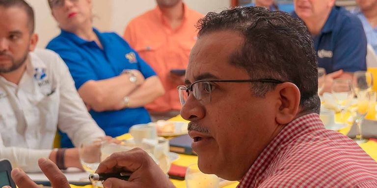 A man in glasses sitting at a table with people in the background
