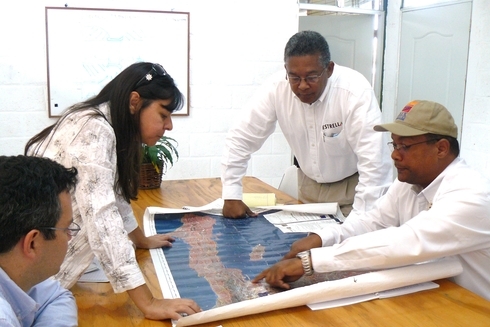 A group of people sitting around a table in a meeting room, discussing a project in Haiti, with a presentation screen visible in the background - Sustainable Development - Inter-American Development Bank - IDB 