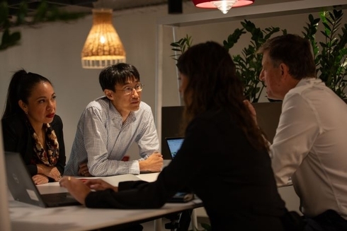A group of four professionals, two men and two women, sit around a table in a modern office space engaged in a serious discussion - Inter-American Development Bank - IDB - Sustainable Development