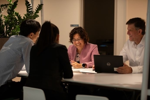 Four professionals sit around a table in a brightly lit office, engaged in a friendly discussion. The setting includes plants in the background, adding to the collaborative and warm atmosphere. Inter-American Development Bank-IDB-Sustainable Development